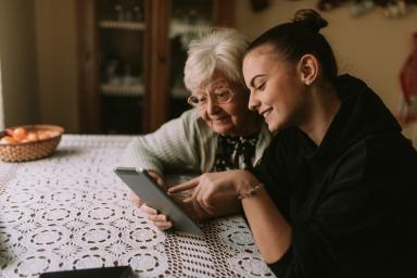 lächelnde junge Frau zeigt älterer Frau etwas auf dem Tablet
