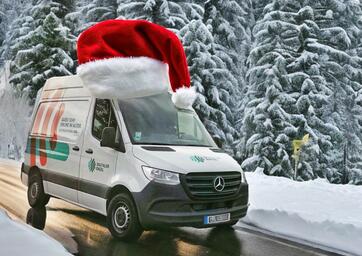 Das Infomobil steht auf einer Stra&szlig;e inmitten von verschneiten B&auml;umen und hat eine Weihnachtsm&uuml;tze auf dem Dach.