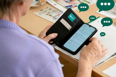 &auml;ltere Person h&auml;lt Smartphone, daneben sind Sprechblasen zu sehen